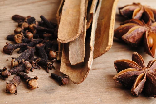 Cinnamon bark, whole cloves and star anise arranged on a wooden board